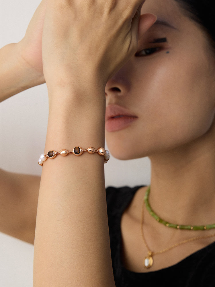 Model wearing a gold-tone pearl and brown stone bracelet with oval settings