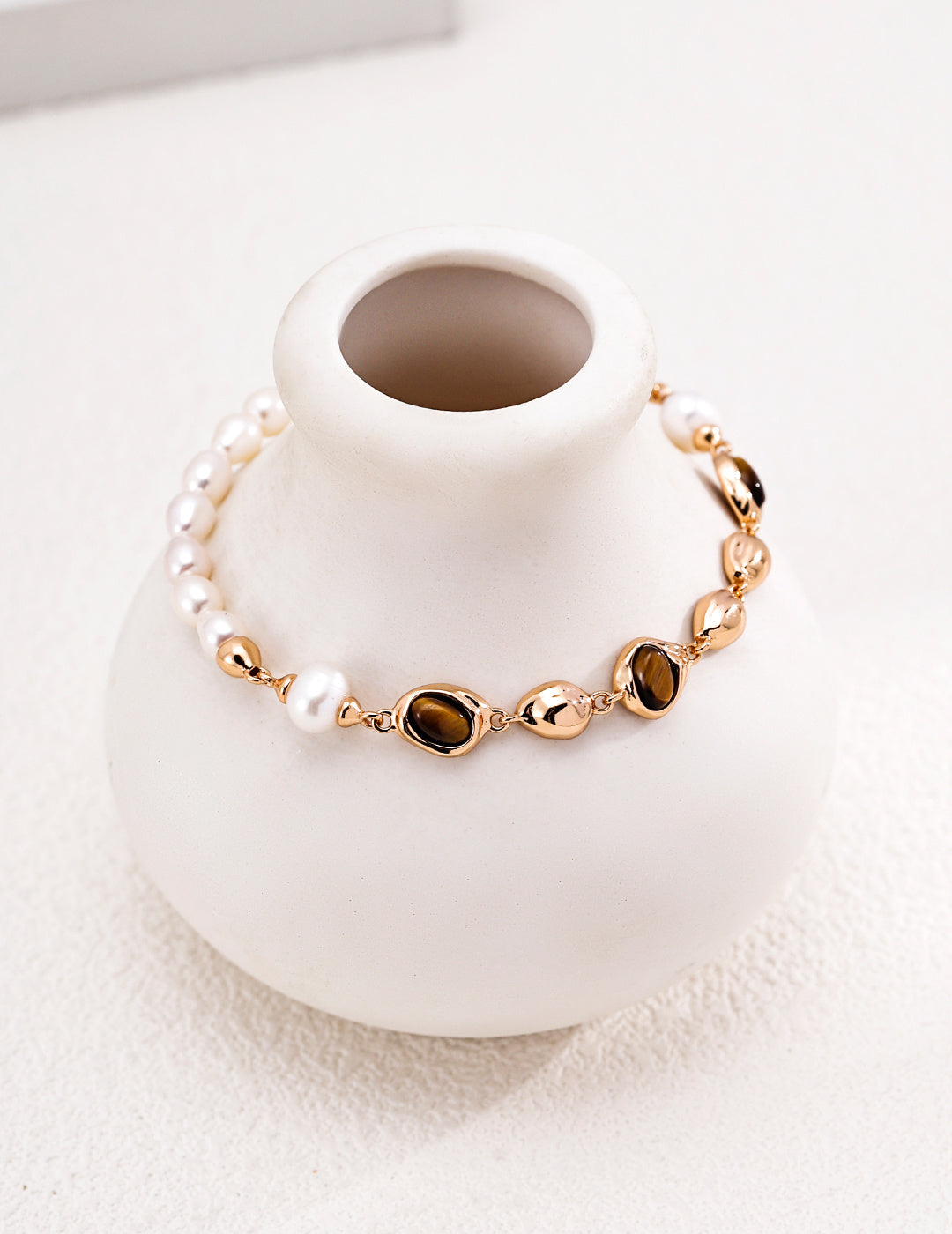 Gold-tone pearl and brown stone bracelet displayed around a white ceramic vase