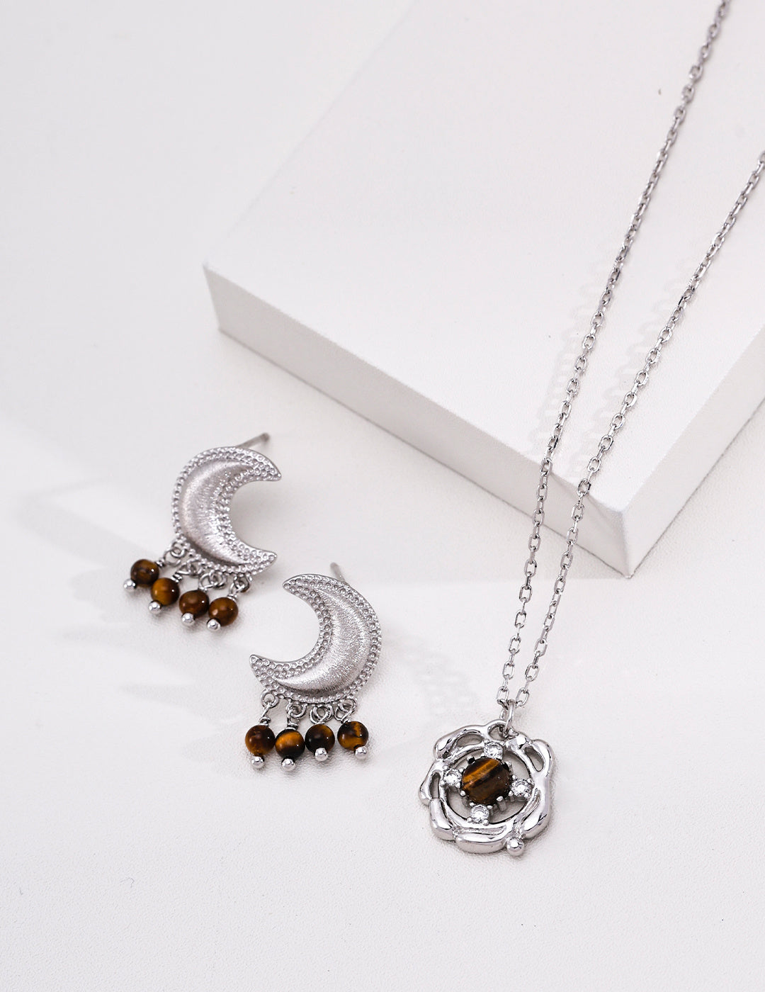 Silver grey crescent moon earrings with tiger’s eye drops displayed beside a matching tiger’s eye pendant necklace