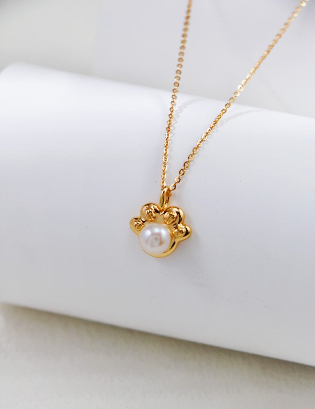 Gold necklace with a pearl pendant on a white surface