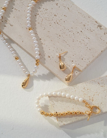 Pearl necklace, bracelet, and earrings on a textured stone surface
