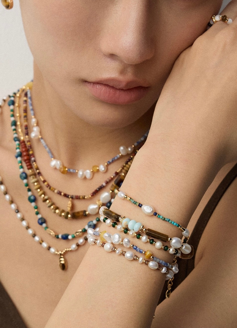 Woman wearing layered pearl and gemstone bracelets with mixed textures