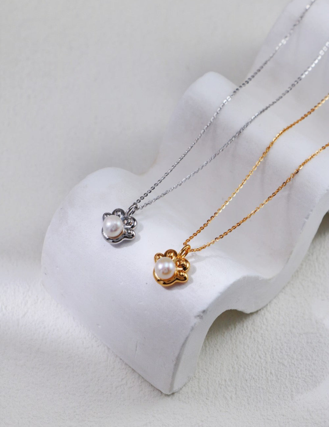 Two pearl necklaces on a white stand with a light gray background
