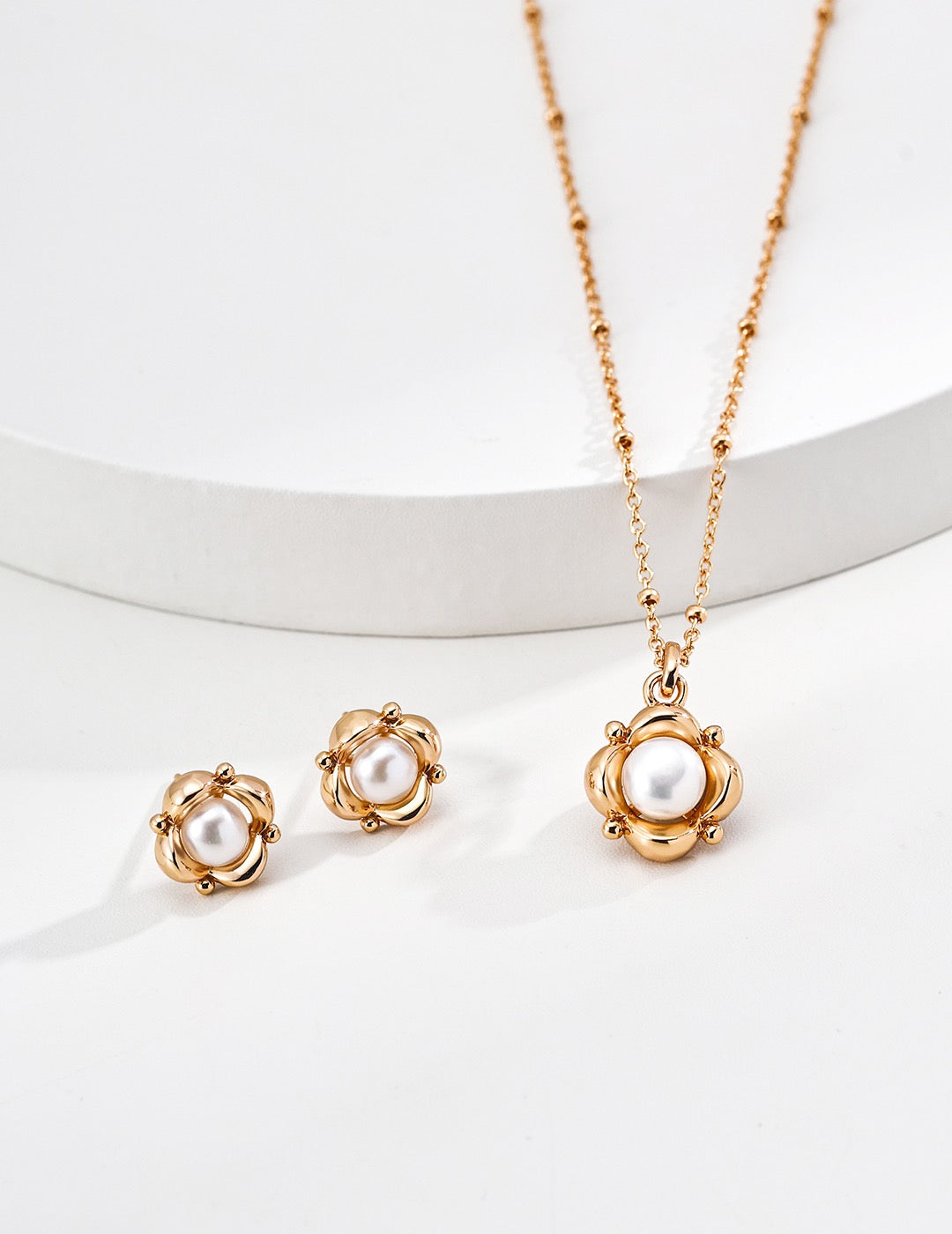 Vintage gold pearl flower stud earrings displayed beside a matching floral pearl pendant necklace