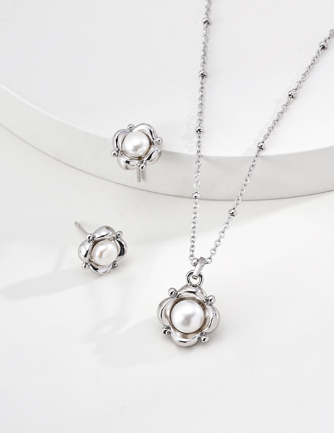 Silver pearl flower stud earrings displayed beside a matching floral pearl pendant necklace