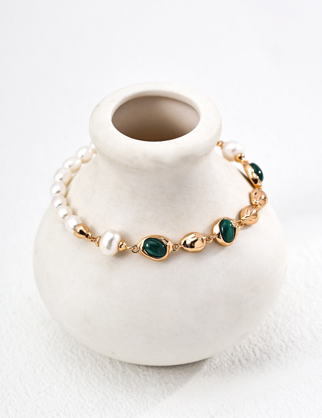 Gold-tone malachite and natural pearl bracelet displayed around a white ceramic vase